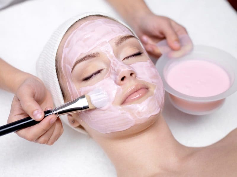 woman getting a facial at spa with pink face mask