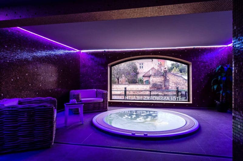 the glassworks spa with a hot tub and dark walls with purple mood lighting
