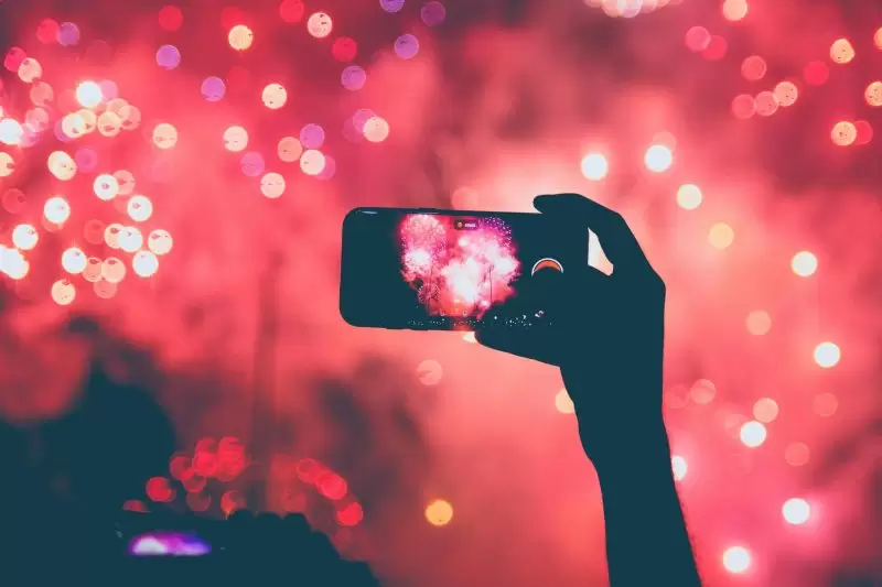 person taking photo of red and pink fireworks in the background