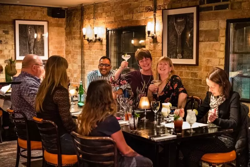 group of people at large table with two friends holding up their cocktails