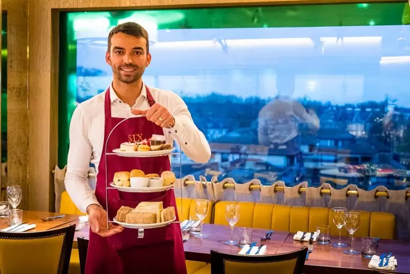 waiter holding an afternoon tea trsy in front of table