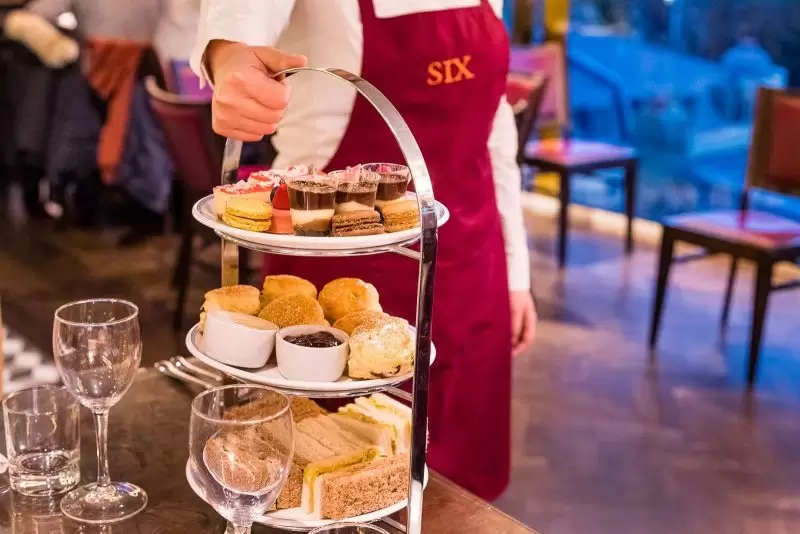 afternoon tea being bought by waitress in a burgundy apron
