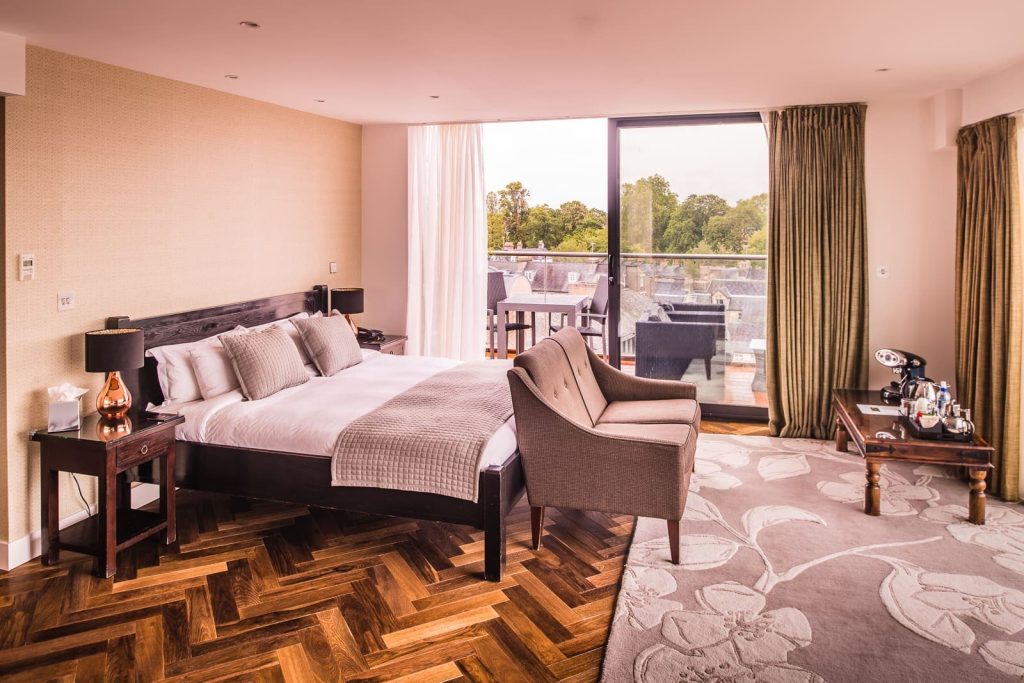 large hotel room with sofa at the end of bed, a coffee machine on table and large balcony