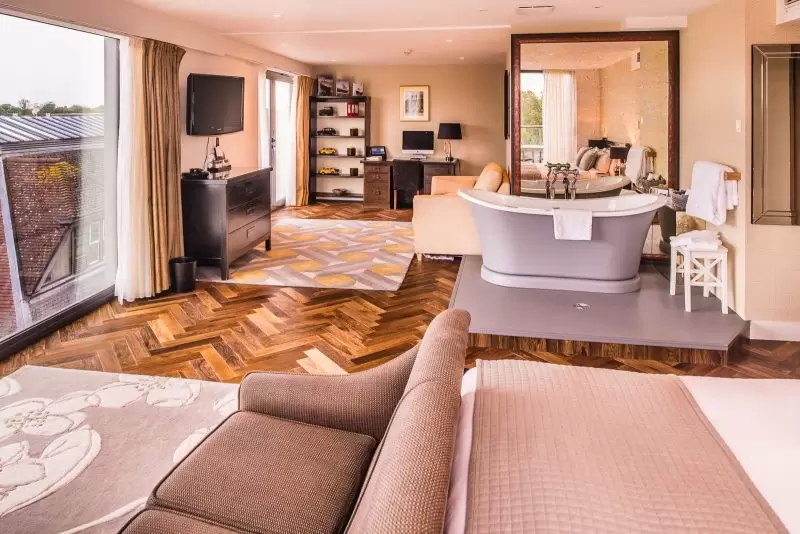 large hotel bedroom with roll top bath and two sofa with floor to ceiling windows