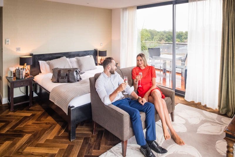 couple sitting on sofa in hotel bedroom drinking a glass of champagne