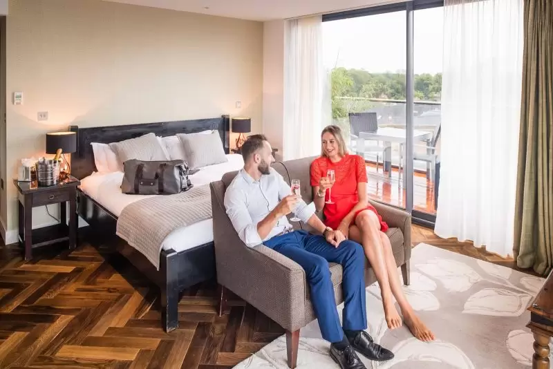 couple sitting on sofa in hotel bedroom drinking a glass of champagne