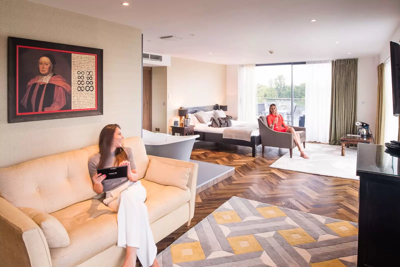 two ladies in hotel bedroom one is looking at the menu the other is drinking champagne