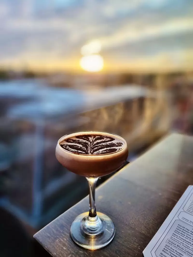 espresso martini on a table with a view of the sunset over cambridge city