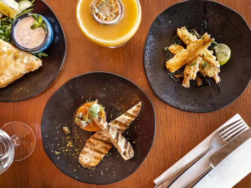 three plates of entrees, calamari, toast and a cocktail