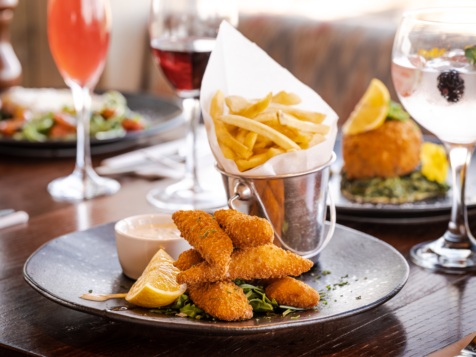 fancy fish fingers with tar tar sauce and a bucket of frieds with a gin and tonic in the background