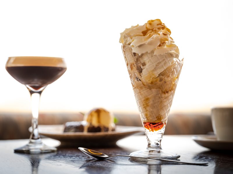dessert on a table, in tall glass, with a brownie and ice cream behind and a tall espresso martini