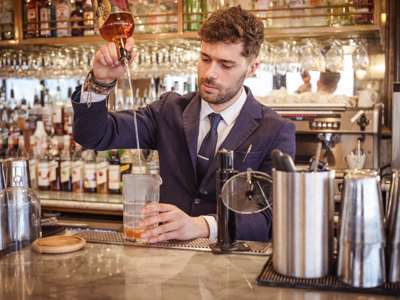 bartender making a cocktail behind the bar pouring into a glass