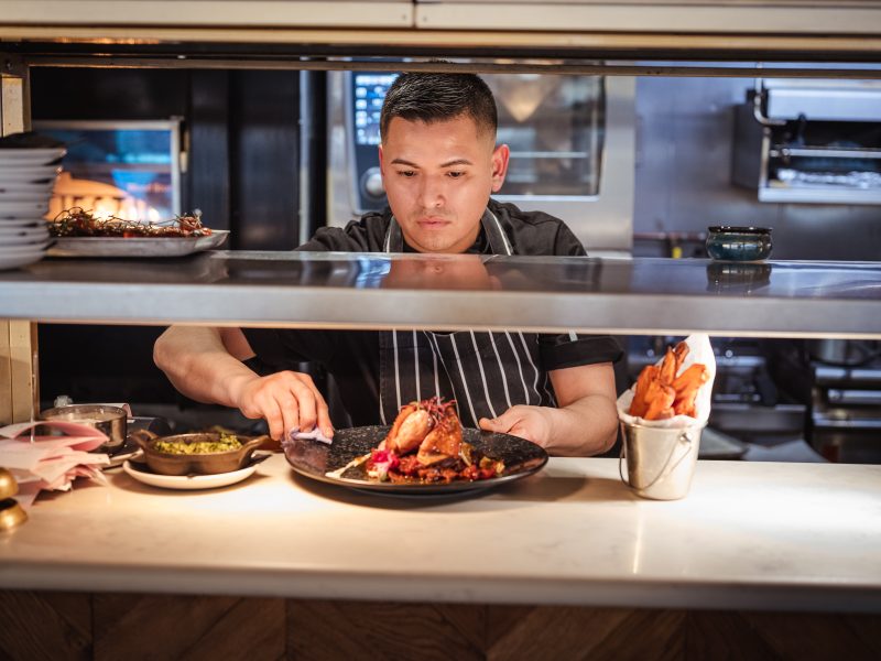 chef cleaning plate in kitchen putting it on the table for waiters to collect