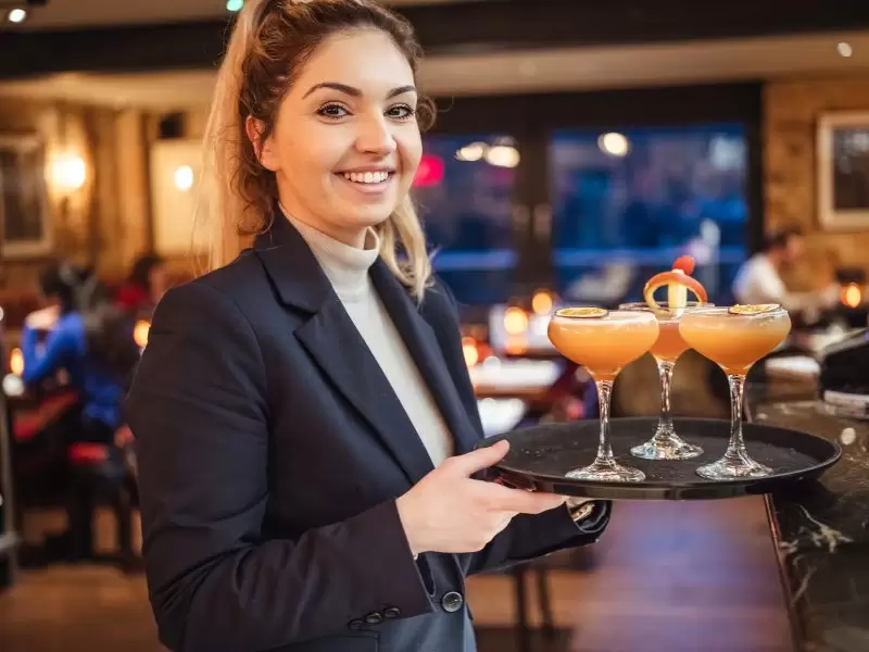 waitress carrying three orange cocktails