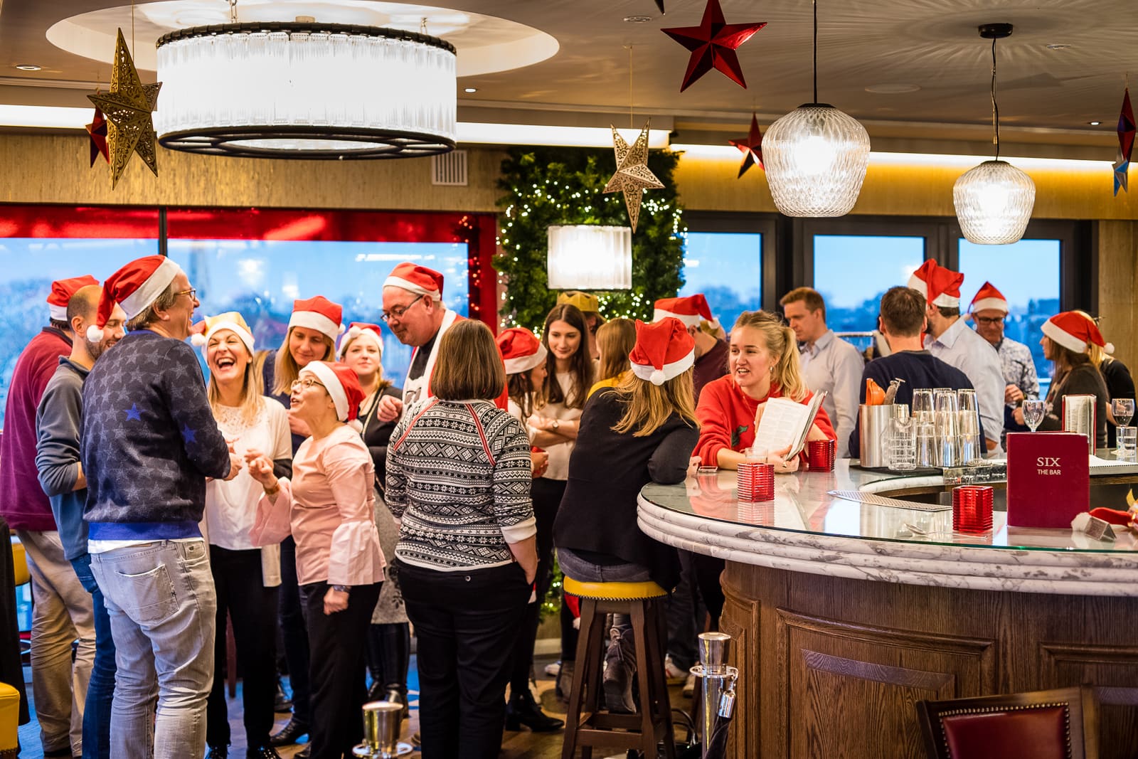 group christmas party standing at the bar wearing christmas hats
