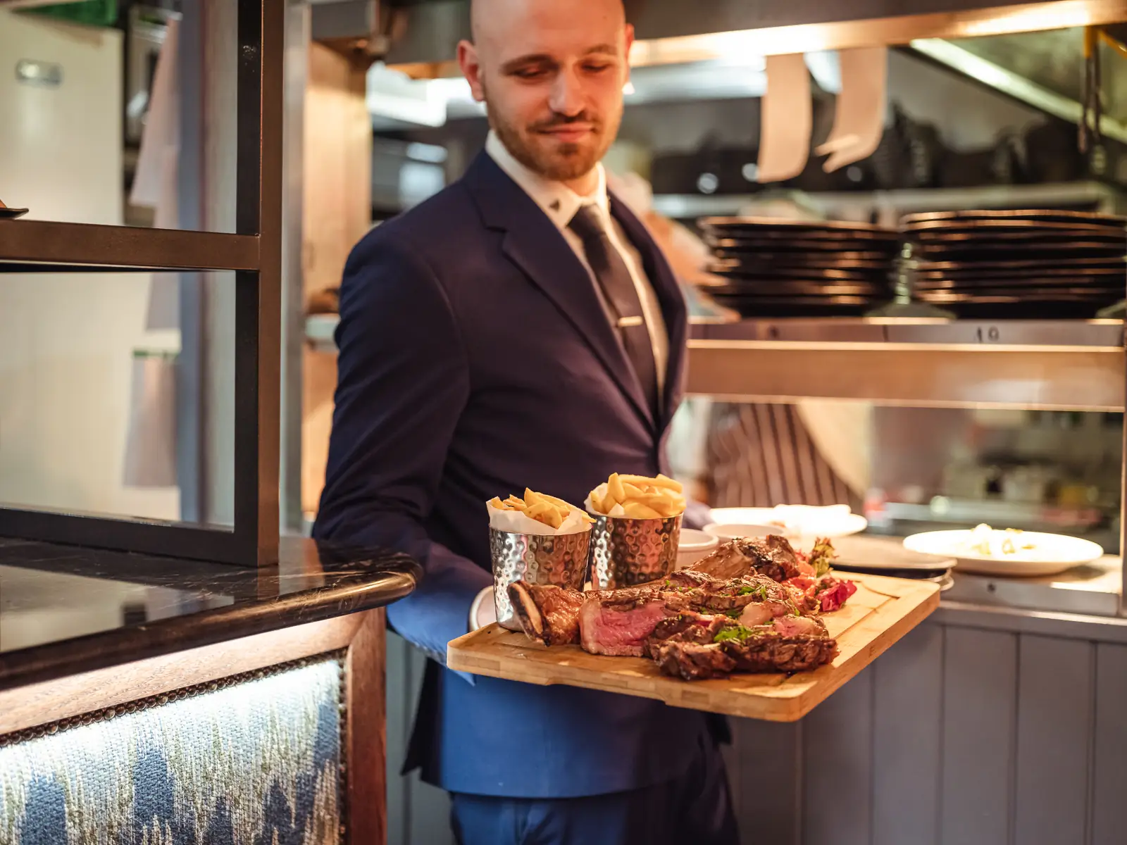 river bar steakhouse waiter holding a steak dinner with chips on wooden board