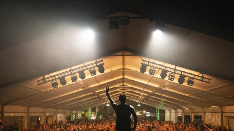 Silhouette of a performer raising his arm in front of a crowded tent at the Cambridge Folk Festival